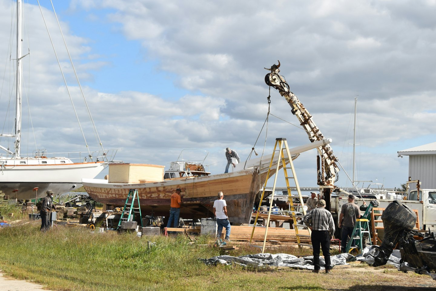 Workers repair a large wooden boat on scaffolding in a boatyard.